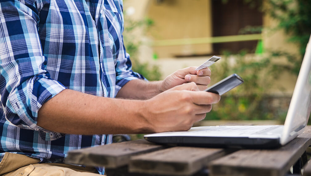 Man using laptop with debit card in hand