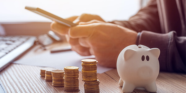 Small piggy bank and coins sitting on table while man uses cell phone in background