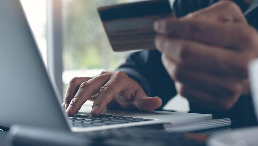 Man typing on computer while holding credit card in other hand