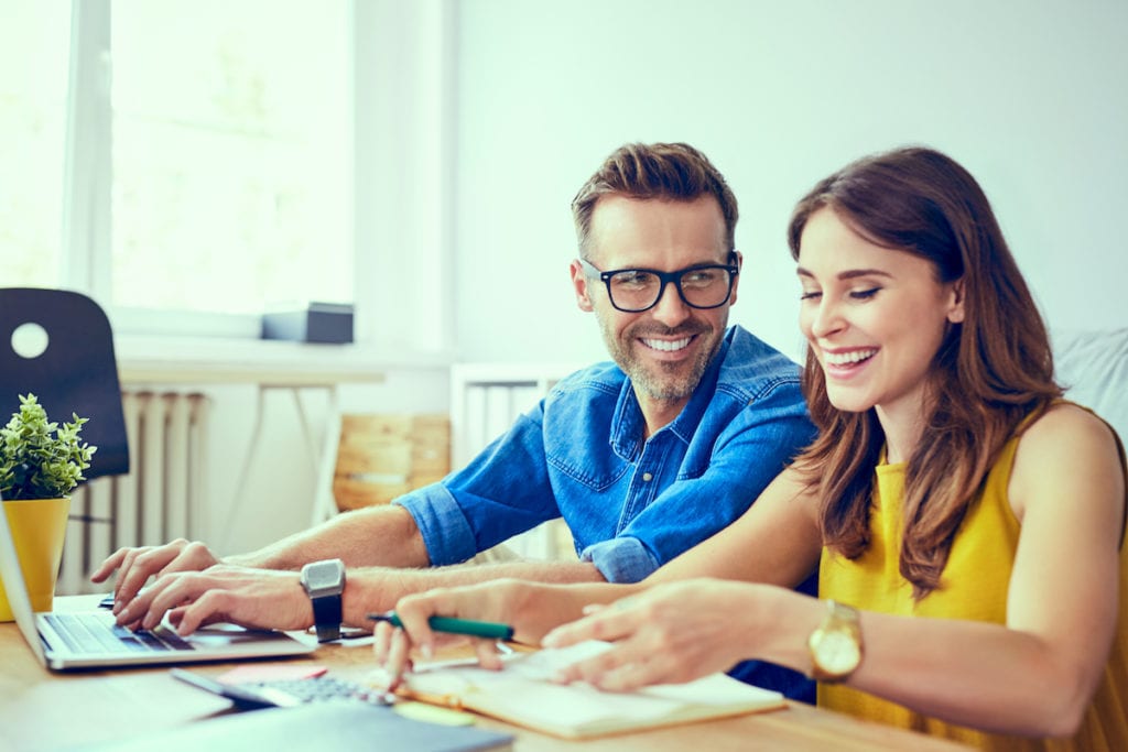 Happy couple sitting at table paying bills with laptop