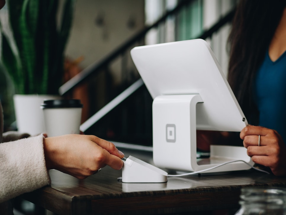 person inserting a credit card into a card reader while person in front of them is behind a monitor taking their payment