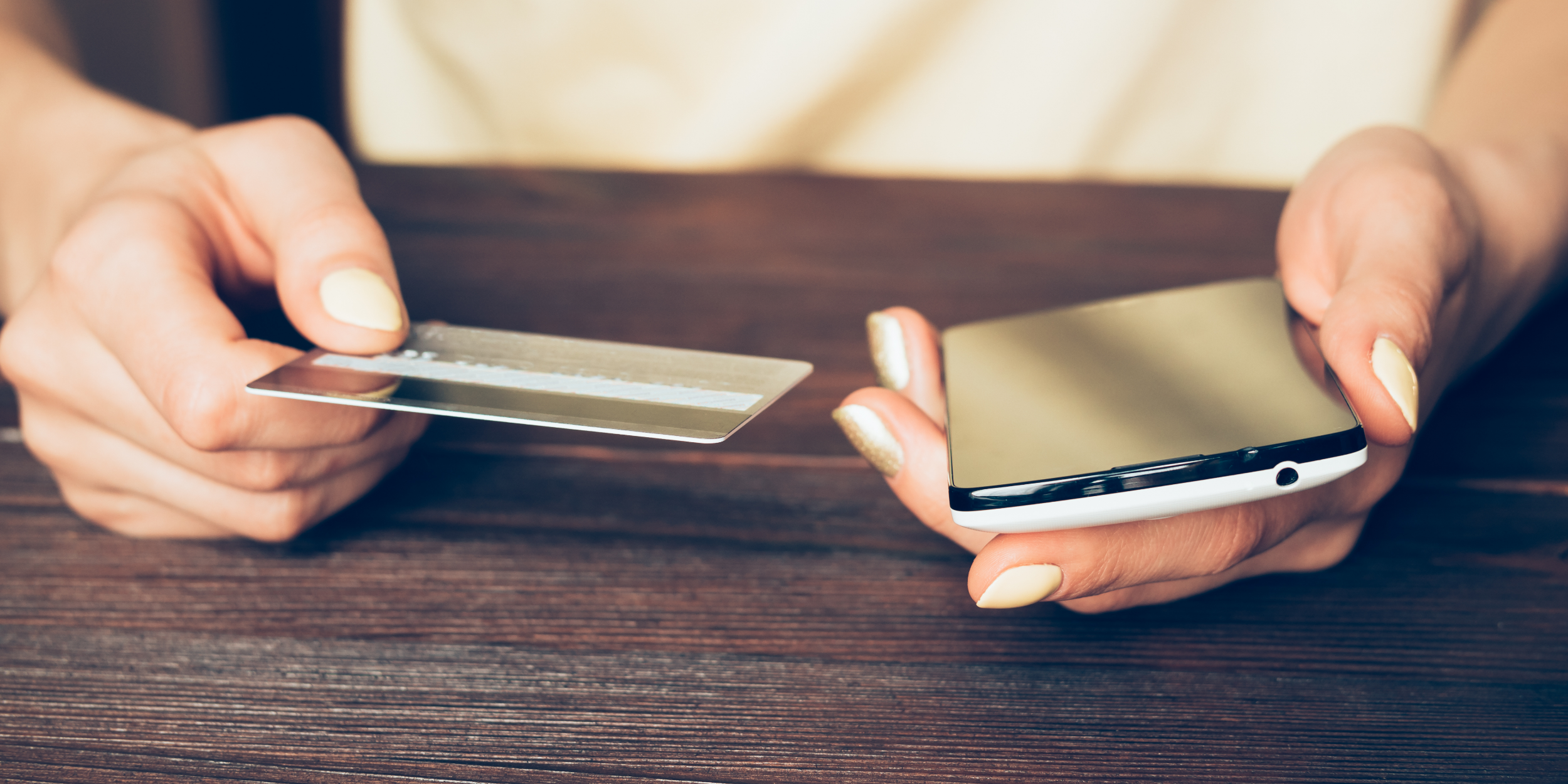 person holding a credit card in one hand and a phone in the other on a table