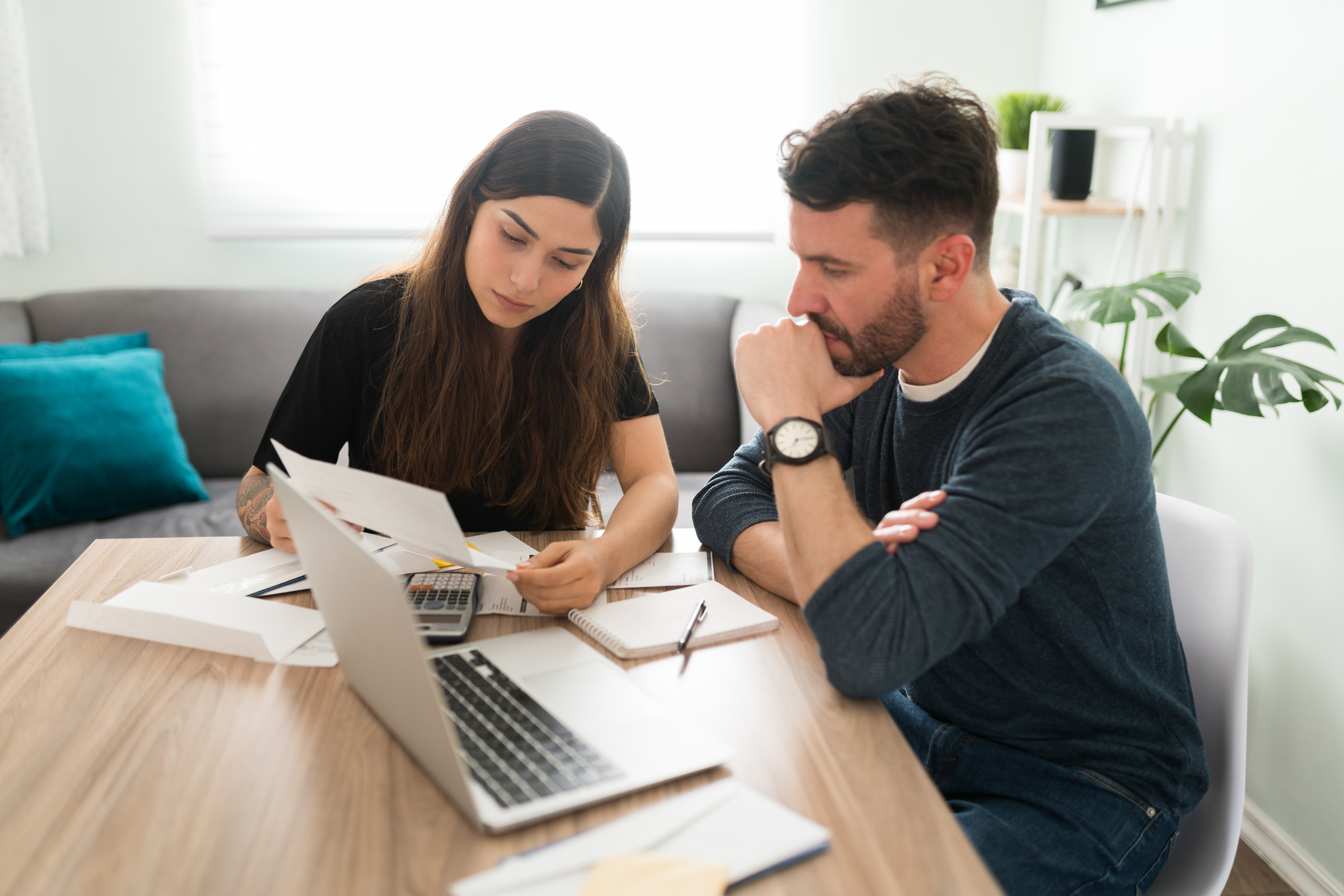 Upset husband and wife doing their taxes with a laptop and bills in their living room. Latin young couple having financial and money problems