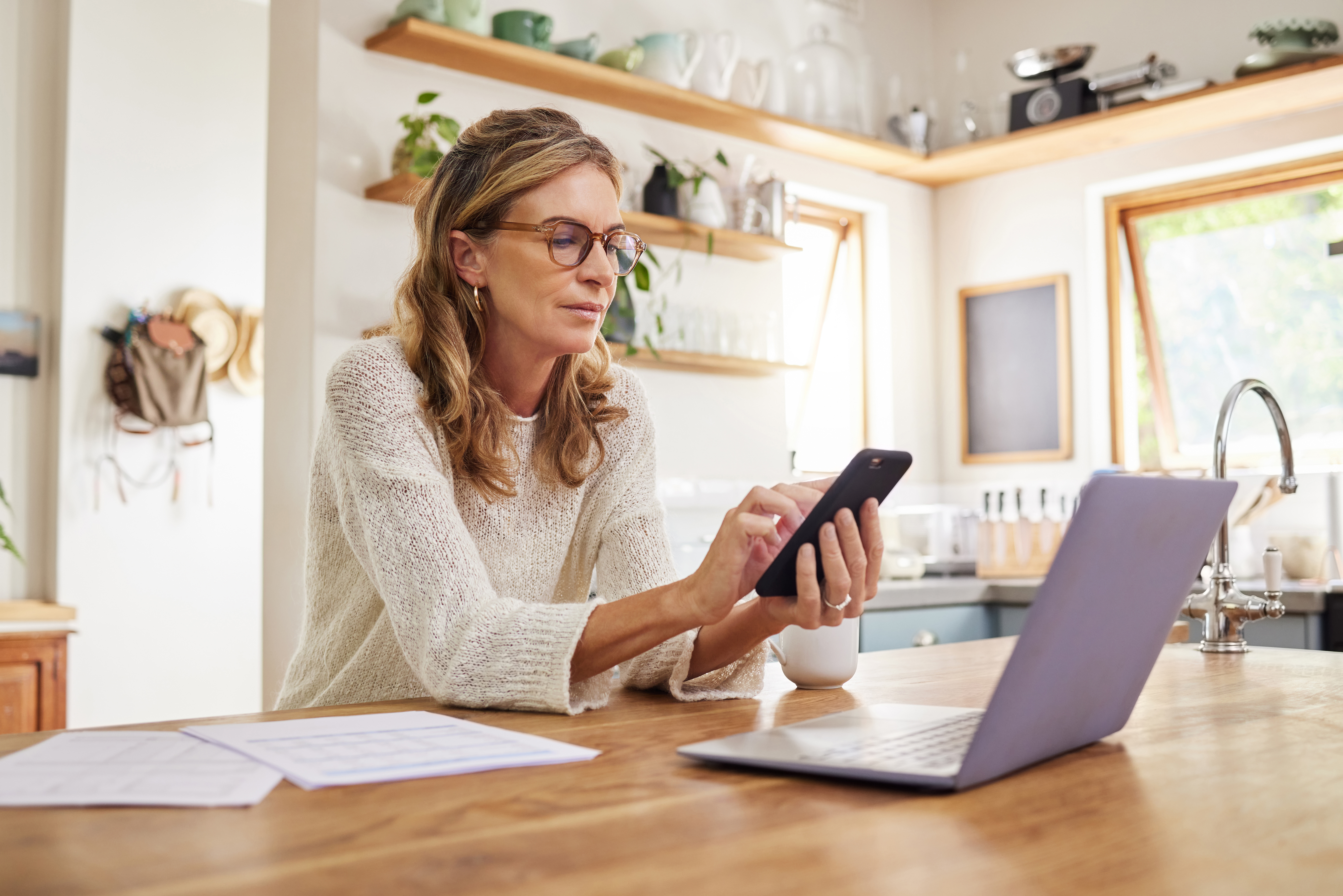 Woman, laptop or fintech phone app in house or home kitchen for finance budget, investment accounting or insurance taxes. Thinking mature person with technology, paper or document for retirement loan.