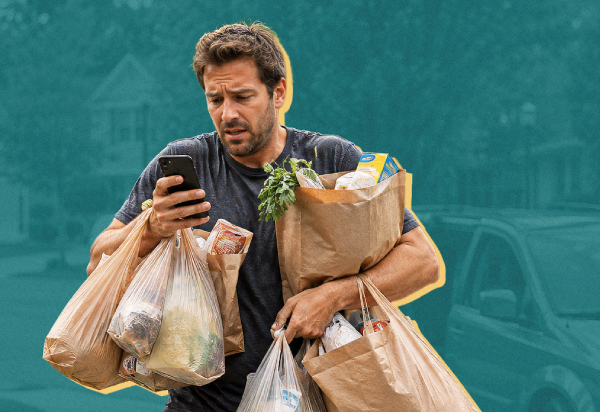 Man juggling many grocery bags and looking at his phone with a concerned expression